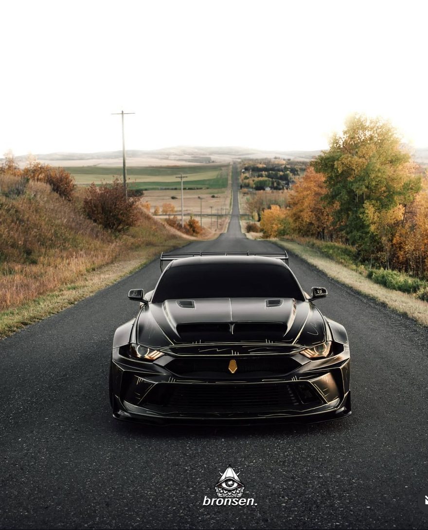 A black widebody Mustang facing down an empty prairie road in autumn